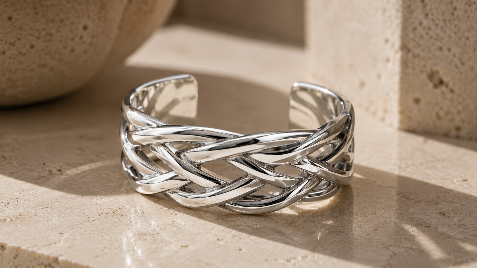 Polished sterling silver braided cuff resting on warm stone